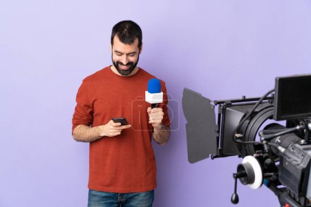 Téléchargez les photos : Reporter homme tenant un microphone et rapportant des nouvelles sur fond violet isolé envoyer un message avec le mobile - en image libre de droit