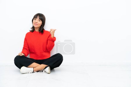 Photo for Young mixed race woman sitting on the floor isolated on white background pointing to the side to present a product - Royalty Free Image