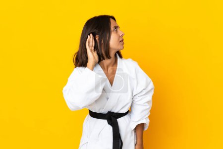 Téléchargez les photos : Jeune femme faisant du karaté isolé sur fond jaune écoutant quelque chose en mettant la main sur l'oreille - en image libre de droit