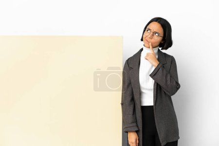Foto de Joven mujer de raza mixta de negocios con una gran pancarta sobre un fondo aislado que tiene dudas mientras mira hacia arriba - Imagen libre de derechos
