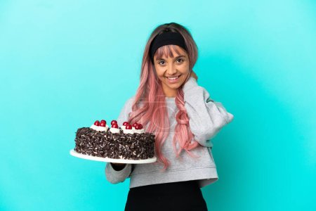 Foto de Mujer joven con cabello rosa sosteniendo pastel de cumpleaños aislado sobre fondo azul riendo - Imagen libre de derechos