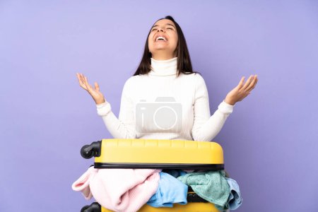 Téléchargez les photos : Voyageur jeune femme avec une valise pleine de vêtements sur fond violet isolé souriant beaucoup - en image libre de droit