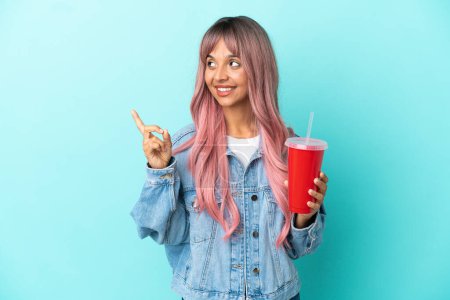 Téléchargez les photos : Jeune femme métisse buvant une boisson fraîche isolée sur fond bleu pointant vers le haut d'une excellente idée - en image libre de droit
