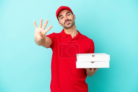 Téléchargez les photos : Livraison homme caucasien ramasser des boîtes de pizza isolé sur fond bleu heureux et comptant quatre avec des doigts - en image libre de droit