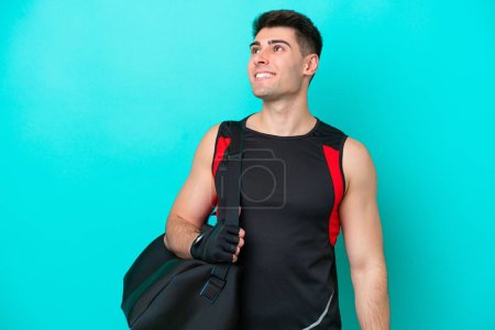 Foto de Joven hombre de deporte caucásico con bolsa de deporte aislado sobre fondo azul pensando una idea mientras mira hacia arriba - Imagen libre de derechos