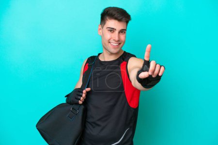 Téléchargez les photos : Jeune homme de sport caucasien avec sac de sport isolé sur fond bleu montrant et levant un doigt - en image libre de droit