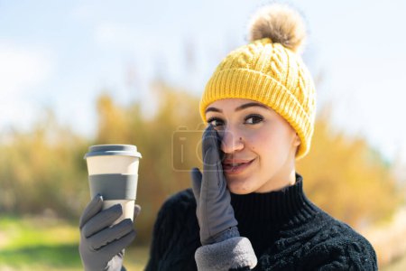 Photo for Young moroccan girl wearing winter muffs while holding a coffee at outdoors whispering something - Royalty Free Image