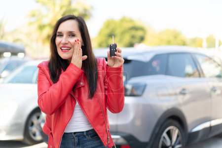 Photo for Middle aged woman holding car keys at outdoors whispering something - Royalty Free Image