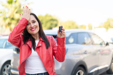 Photo for Middle aged woman holding car keys at outdoors has realized something and intending the solution - Royalty Free Image
