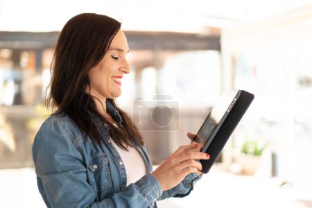 Téléchargez les photos : Femme d'âge moyen touchant l'écran de la tablette avec une expression heureuse - en image libre de droit