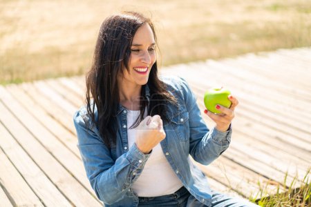 Photo for Middle aged woman with an apple at outdoors celebrating a victory - Royalty Free Image