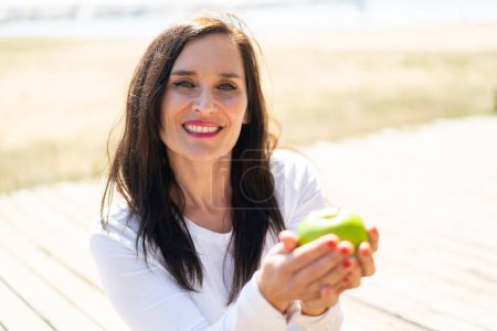 Téléchargez les photos : Femme d'âge moyen tenant une pomme avec une expression heureuse - en image libre de droit