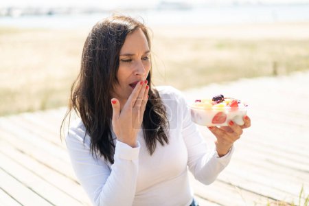 Photo for Middle aged woman holding a bowl of fruit at outdoors with surprise and shocked facial expression - Royalty Free Image