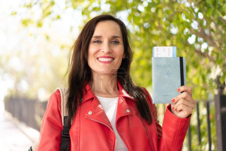 Foto de Mujer de mediana edad sosteniendo un pasaporte al aire libre sonriendo mucho - Imagen libre de derechos