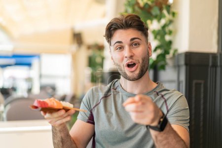 Téléchargez les photos : Jeune homme beau tenant sashimi à l'extérieur surpris et pointant devant - en image libre de droit