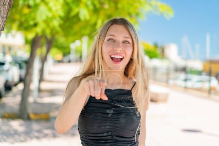 Téléchargez les photos : Jeune femme blonde à l'extérieur surpris et pointant devant - en image libre de droit