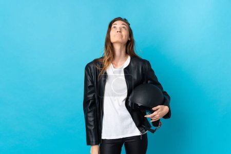 Téléchargez les photos : Jeune Irlandaise tenant un casque de moto isolé sur fond bleu et levant les yeux - en image libre de droit