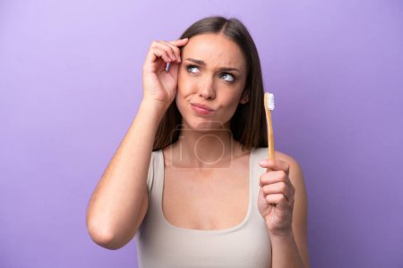 Photo for Young caucasian woman brushing teeth isolated on purple background having doubts and with confuse face expression - Royalty Free Image