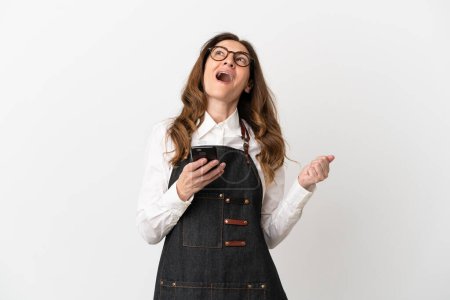 Téléchargez les photos : Restaurant femme serveur d'âge moyen isolé sur fond blanc avec téléphone en position de victoire - en image libre de droit