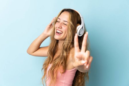 Foto de Mujer rubia joven aislada sobre fondo azul escuchando música y cantando - Imagen libre de derechos