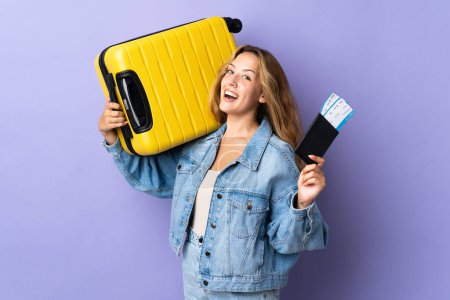 Téléchargez les photos : Jeune femme blonde isolée sur fond violet en vacances avec valise et passeport - en image libre de droit