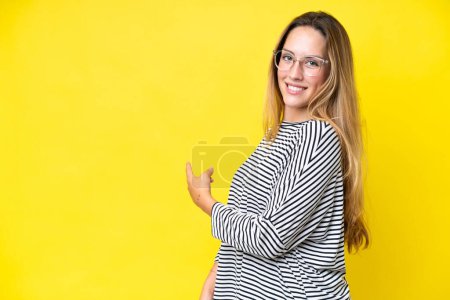 Foto de Mujer joven caucásica aislada sobre fondo amarillo apuntando hacia atrás - Imagen libre de derechos
