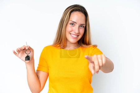 Foto de Joven mujer caucásica sosteniendo llaves de casa aisladas sobre fondo blanco señala el dedo en usted con una expresión de confianza - Imagen libre de derechos