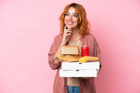 Téléchargez les photos : Jeune femme caucasienne tenant fast food isolé sur fond rose penser une idée tout en levant les yeux - en image libre de droit