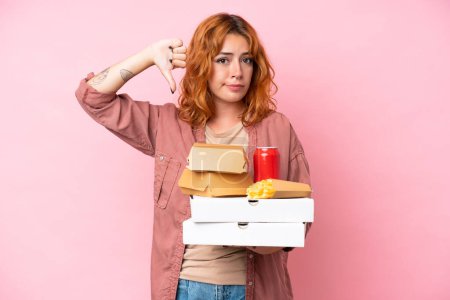 Téléchargez les photos : Jeune femme caucasienne tenant fast food isolé sur fond rose montrant pouce vers le bas avec expression négative - en image libre de droit
