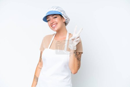 Photo for Fishmonger wearing an apron and holding a raw fish isolated on white background smiling and showing victory sign - Royalty Free Image