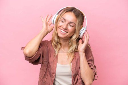 Foto de Young Russian woman isolated on pink background listening music and singing - Imagen libre de derechos