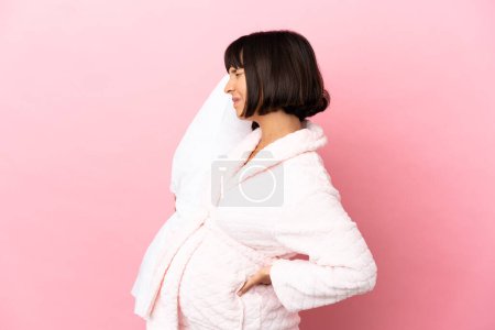 Foto de Mujer embarazada en pijama aislada sobre fondo rosa que sufre de dolor de espalda por haber hecho un esfuerzo - Imagen libre de derechos
