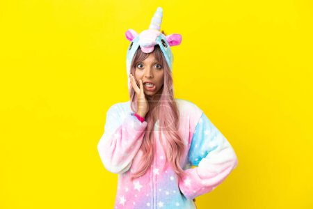 Foto de Mujer joven de raza mixta con un pijama unicornio aislado sobre fondo blanco con expresión facial sorpresa y conmocionada - Imagen libre de derechos