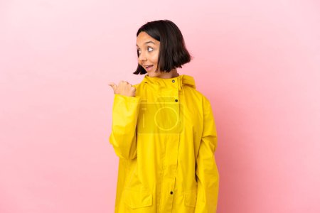Photo for Young latin woman wearing a rainproof coat over isolated background pointing to the side to present a product - Royalty Free Image