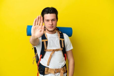 Photo for Young mountaineer Russian man with a big backpack isolated on yellow background making stop gesture - Royalty Free Image