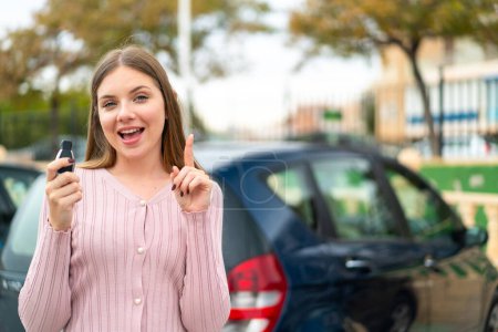 Foto de Joven mujer rubia bonita sosteniendo las llaves del coche al aire libre señalando una gran idea - Imagen libre de derechos