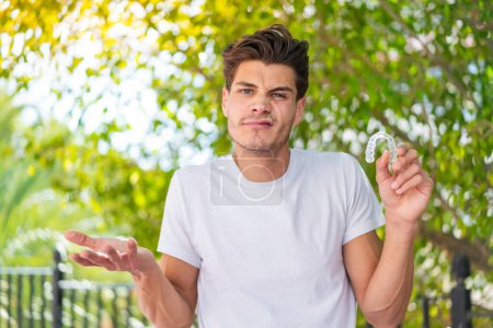 Photo for Young caucasian man holding invisible braces at outdoors making doubts gesture while lifting the shoulders - Royalty Free Image