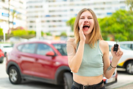 Téléchargez les photos : Jeune femme blonde tenant des clés de voiture à l'extérieur criant avec la bouche grande ouverte - en image libre de droit