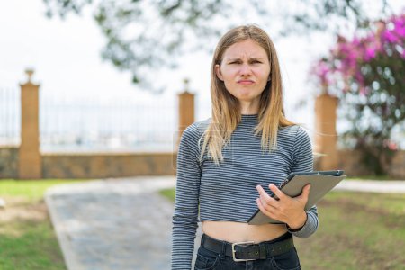 Photo for Young blonde woman holding a tablet at outdoors with sad expression - Royalty Free Image