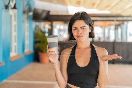 Photo for Young pretty Bulgarian woman holding a take away coffee at outdoors making doubts gesture while lifting the shoulders - Royalty Free Image