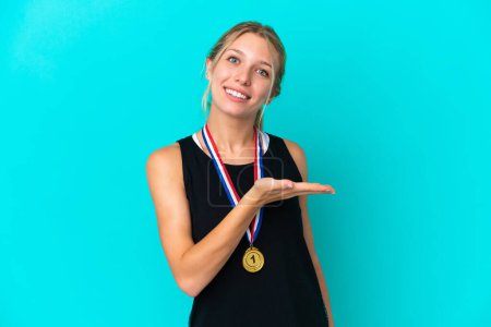 Foto de Mujer joven caucásica con medallas aisladas sobre fondo azul presentando una idea mientras mira sonriendo hacia - Imagen libre de derechos