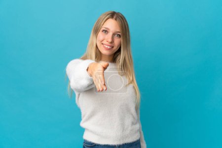 Téléchargez les photos : Jeune femme blonde isolée sur fond bleu serrant la main pour conclure une bonne affaire - en image libre de droit