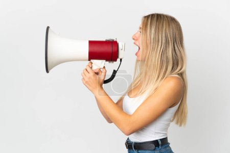 Photo for Young blonde woman isolated on white background shouting through a megaphone to announce something in lateral position - Royalty Free Image