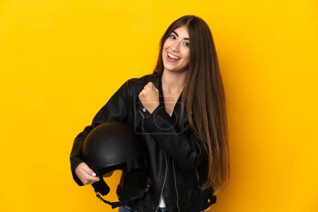 Photo for Young caucasian woman holding a motorcycle helmet isolated on yellow background celebrating a victory - Royalty Free Image