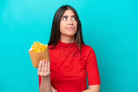 Téléchargez les photos : Jeune femme caucasienne attrapant des frites isolées sur fond bleu et levant les yeux - en image libre de droit