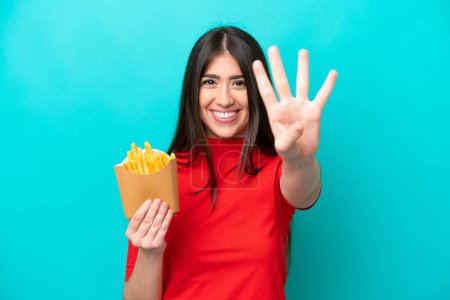 Foto de Joven mujer caucásica atrapando papas fritas aisladas sobre fondo azul feliz y contando cuatro con los dedos - Imagen libre de derechos