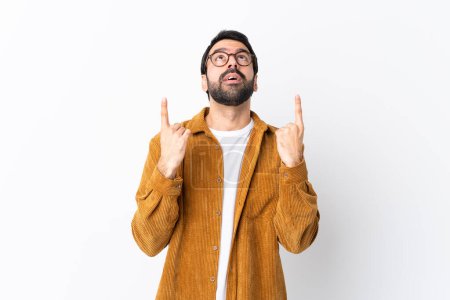 Foto de Caucásico hombre guapo con barba usando una chaqueta de pana sobre fondo blanco aislado sorprendido y señalando hacia arriba - Imagen libre de derechos