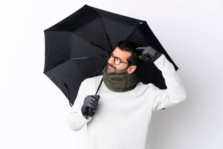 Téléchargez les photos : Homme beau caucasien avec barbe tenant un parapluie sur mur blanc isolé ayant des doutes tout en grattant la tête - en image libre de droit
