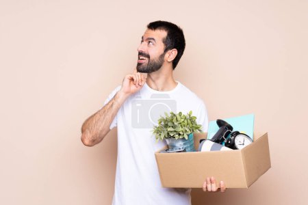 Téléchargez les photos : Homme tenant une boîte et déménageant dans une nouvelle maison sur fond isolé penser une idée tout en levant les yeux - en image libre de droit