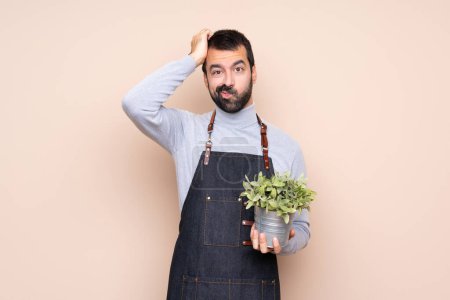 Téléchargez les photos : Homme tenant une plante sur fond isolé avec une expression de frustration et de ne pas comprendre - en image libre de droit